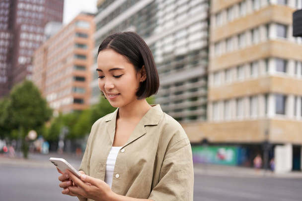 Jeune femme asiatique explorer la ville avec application smartphone, tenant téléphone mobile et marcher sur un écran. - Photo, image