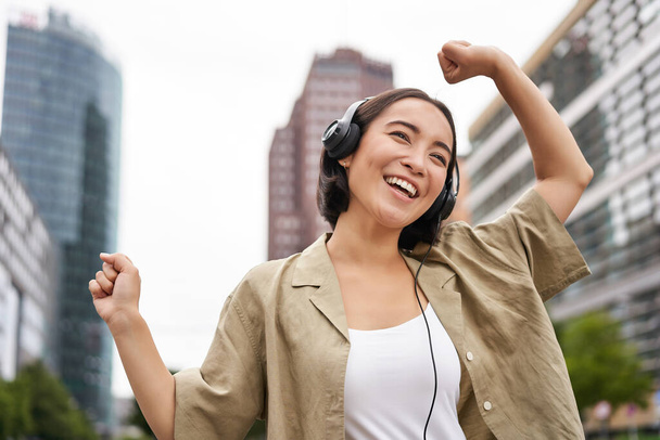 Taniec azjatycki dziewczyna słuchanie muzyki w słuchawki, uczucie szczęśliwy w mieście, korzystających na świeżym powietrzu. - Zdjęcie, obraz