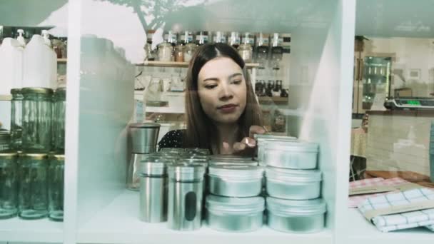 Молода кавказька жінка-крамарка працює, організовуючи багаторазові продукти на віконних виставках у магазинах, нульових відходах, пластмасових товарах і екологічно дружній роздрібній торгівлі стартап. - Кадри, відео