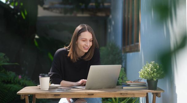 Attraktive junge Frau im warmen Pullover surft auf Laptop im Internet, während sie im Freien sitzt. - Foto, Bild