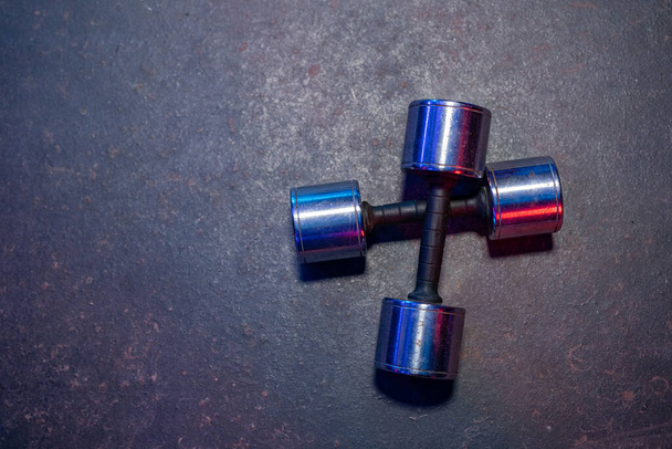 Metallic silvery dumbbells lying on the gray floor in the gym. Two barbells with reflective red and blue lights. Top view of equipment for sports, bodybuilding or crossfit. Fitness, strength training - Photo, Image