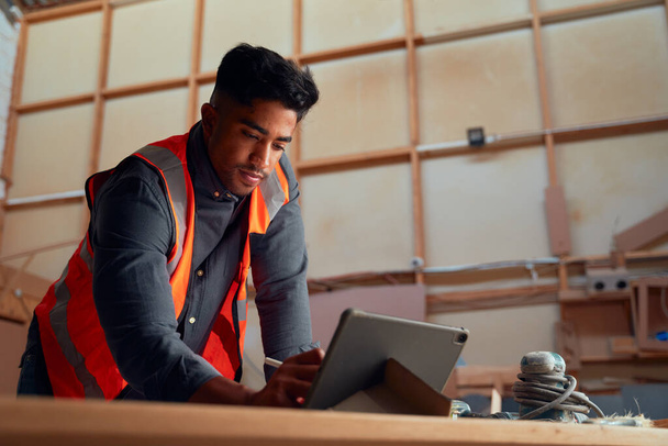 Multiracial young man wearing reflective clothing using digitized pen on digital tablet in woodworking factory - Zdjęcie, obraz