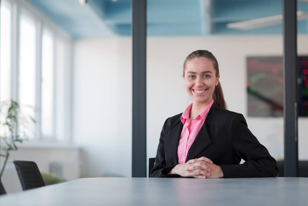 Successful young female leader in a suit with a pink shirt sitting in a modern glass office with a determined smile.Concept of business and the success of young people in modern online businesses  - Photo, Image