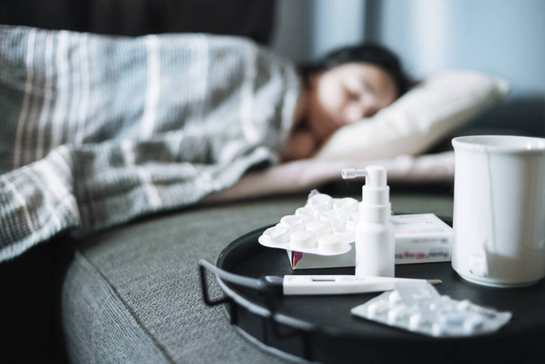 季節の寒さに苦しむ少女がベッドに横たわっている。トレイ上の抗ウイルス薬 - 写真・画像