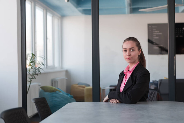 Successful young female leader in a suit with a pink shirt sitting in a modern glass office with a determined smile.Concept of business and the success of young people in modern online businesses  - Photo, image