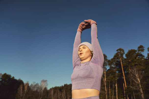 Χαμηλή γωνία της ξανθιάς καυκάσιας γυναίκας ζέσταμα το χειμώνα έξω με τα χέρια ψηλά  - Φωτογραφία, εικόνα