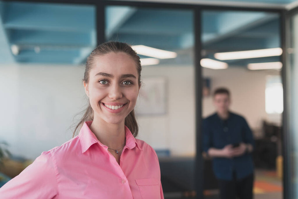 Portrait of young smiling business woman in creative open space coworking startup office. Successful businesswoman standing in office with copyspace. Coworkers working in background - Fotoğraf, Görsel