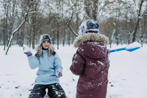 Kültéri téli tevékenységek gyerekeknek és családoknak. Hadd essen a hó. Boldog család Anya és fia jól érzik magukat, futnak, együtt hógolyóznak a téli havas parkban. - Fotó, kép