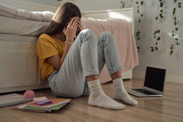blank tiener meisje zitten op de vloer met hoofd in de handen en proberen om te leren - Foto, afbeelding