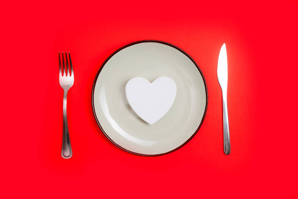 Ρομαντική ιδέα του Αγίου Βαλεντίνου για δείπνο. Καρδιά στο πιάτο και ασημένια φθορά σε κόκκινο φόντο. - Φωτογραφία, εικόνα