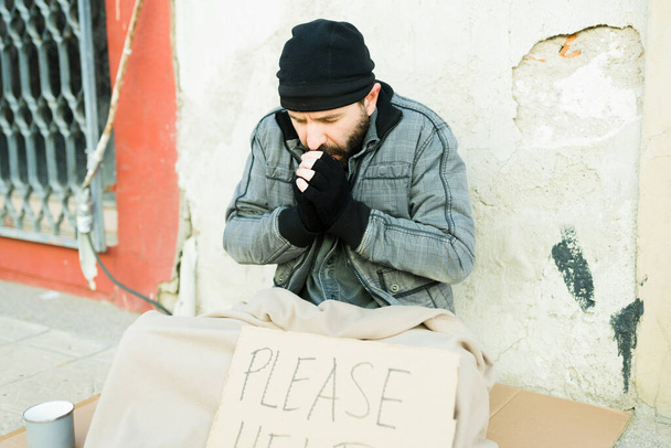 Холодный бездомный греет руки в перчатках и держит знак, пожалуйста, помогите  - Фото, изображение