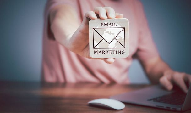 Concept de marketing par courriel, Homme utilisant un ordinateur portable et tenant une plaque en bois avec icône e-mail et écriture Texte de marketing par courriel. - Photo, image