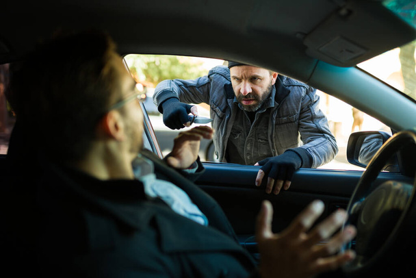 Злий безпритульний злочинець у бідності грабує чоловіка в машині ножем, щоб купити їжу
 - Фото, зображення