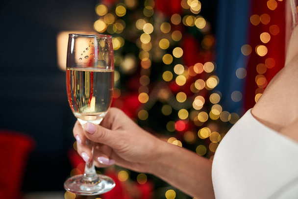 Close up of blonde, seductive woman holding glass of champagne, cheering. Attractive, young lady wearing white dress, posing indoors. Concept of New Year and celebration. - Valokuva, kuva