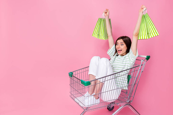 Full length photo of surprised customer sit trolley look empty space celebrate good shopping purchase isolated on pink color background. - Φωτογραφία, εικόνα