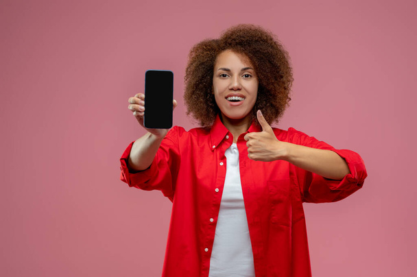 Gadget. Junge Frau mit lockigem Haar und Smartphone in der Hand - Foto, Bild