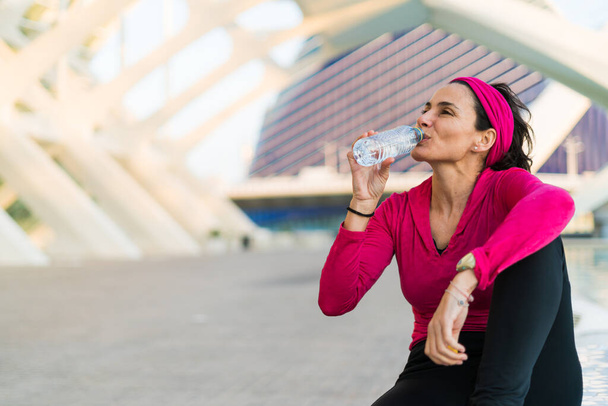 Young adult woman drinking water resting from workout - Zdjęcie, obraz
