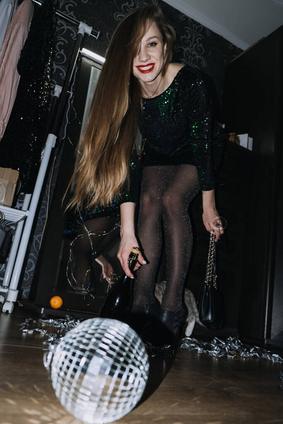 Nightlife, Birthday, New Year Eve party. Beautiful woman in shiny evening dress is going to Birthday New Years Eve party. Young beautiful girl playing with the kitten mirror ball at home. - Foto, Imagem