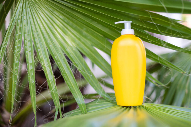 Flacon cosmétique jaune sur le gros plan de la feuille de palmier. Maquette. Cosmétiques ou vacances d'été concept. - Photo, image