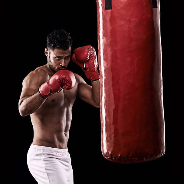 The focussed professional. Studio shot of handsome young man and his punching bag against a black background - Photo, Image
