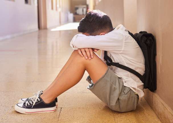 Anxiety, school and sad student bullying victim feeling depression, lost or stressed in hallway or corridor floor. Child, depressed boy or lonely male learner crying alone with abuse trauma or fear. - 写真・画像
