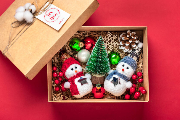 手作りケアパッケージ、おもちゃ付きの季節のギフトボックス、赤いテーブルの上のクリスマスの装飾家族、友人、 24 12月の女の子のためのパーソナライズされた環境に優しいバスケット、クリスマス、新年フラットレイ. - 写真・画像