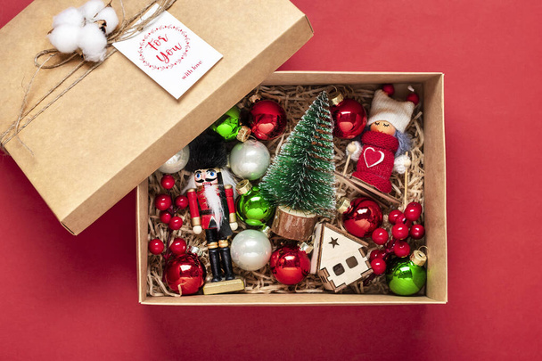 手作りケアパッケージ、おもちゃ付きの季節のギフトボックス、赤いテーブルの上のクリスマスの装飾家族、友人、 24 12月の女の子のためのパーソナライズされた環境に優しいバスケット、クリスマス、新年フラットレイ. - 写真・画像