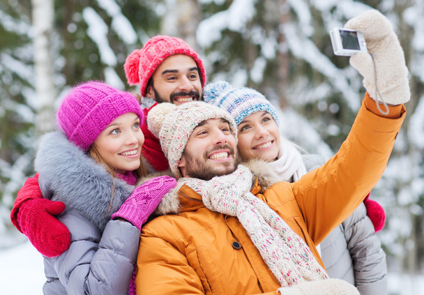 smiling friends with camera in winter forest - Foto, Imagen