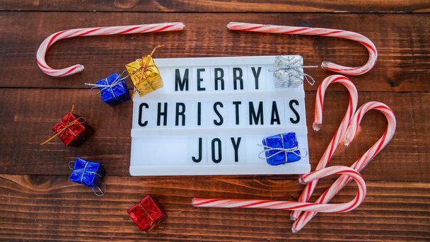 Merry Christmas text in light box with gifts around on wooden table from above - Φωτογραφία, εικόνα