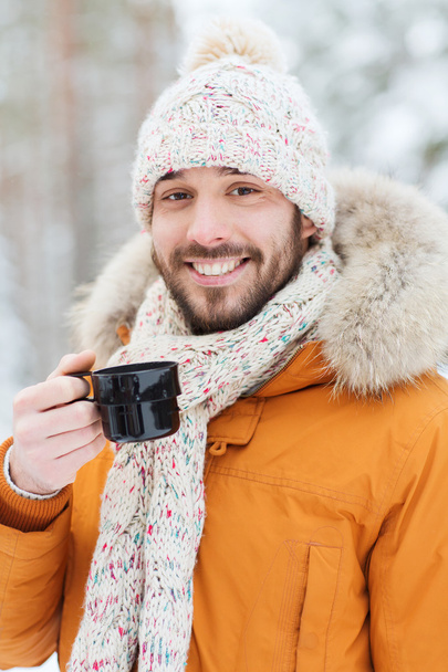 smiling young man with cup in winter forest - Fotoğraf, Görsel