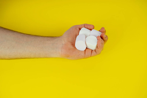 Stapel marshmallow op korte man hand, geïsoleerd op gele achtergrond, marshmallow dienen met de hand, camping food concept - Foto, afbeelding