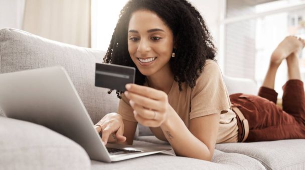 Кредитная карта, ноутбук и интернет-магазины с черной женщиной-клиентом, лежащей на диване в гостиной своего дома. Компьютер, электронная коммерция и розничная торговля с женщиной потребительских расходов деньги в Интернете. - Фото, изображение