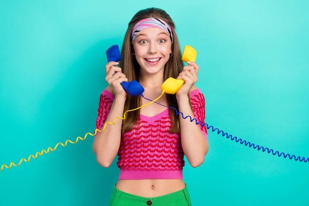 Portrait of impressed positive ecstatic girl with brown hair dressed pink top hold landline phones isolated on teal color background. - Fotoğraf, Görsel
