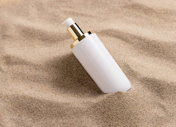 En blanco una bomba Botella de crema con etiqueta en blanco en arena beige de cerca. Maqueta de empaquetado cosmético. Producto de cuidado de la piel natural para la rutina de belleza. Vacaciones tropicales de verano - Foto, Imagen