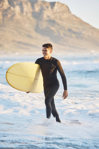 Surfing sports and man walking from ocean with smile, surfboard in hand and happiness in summer. Nature, water sports and male surfer on beach shore after fitness, exercise and cardio for wellness. - Photo, Image