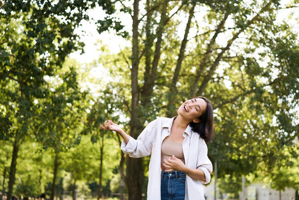 Boldog fiatal ázsiai nő sétál egyedül, táncol és énekel a parkban, vigyorog gondtalanul. Az emberek és az életmód fogalma. - Fotó, kép
