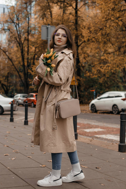 Beautiful young woman with glasses walking in the city. Outdoor portrait of lovable trendy lady with brown hair wears hat in autumn day. - Valokuva, kuva