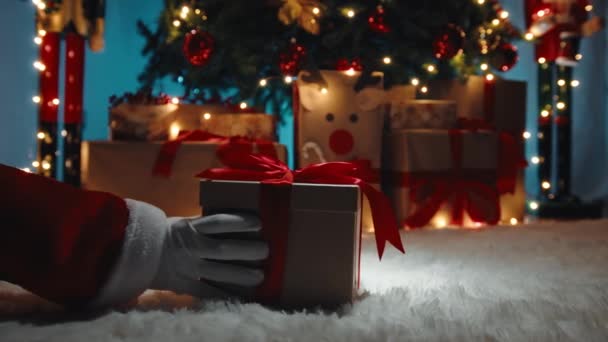 Mano de Santa Claus i entregar la caja de regalo de Navidad bajo el árbol en la noche. - Imágenes, Vídeo