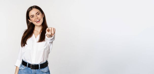 Sebevědomá mladá korporátní žena ukazuje prsty na fotoaparát, zve, vybírá, gratuluje, stojí nad bílým pozadím. - Fotografie, Obrázek