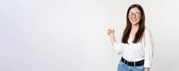 Smiling brunette woman, office lady showing way, pointing behind, demonstrating smth behind her, standing over white background. - Foto, afbeelding