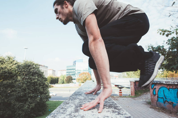 Jongeman in sportieve kleding workout buiten doen parkour springen over obstakel - Foto, afbeelding