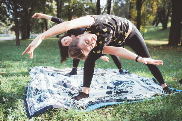 Spor formundaki atletik kadınlar sabah yoga yapıyor açık hava parkında birlikte antrenman yapıyorlar. - Fotoğraf, Görsel