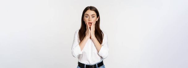 Surprised brunette woman looking amazed, seeing smth awesome, standing in blouse and jeans over white background. - Foto, Bild
