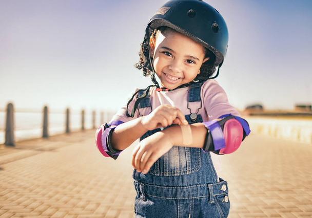 Skating injury, first aid or child portrait with bandage bruise from skate, cycling or accident in street. Happy, smile or girl with helmet for exercise, wellness health at beach, sea or ocean. - Fotoğraf, Görsel