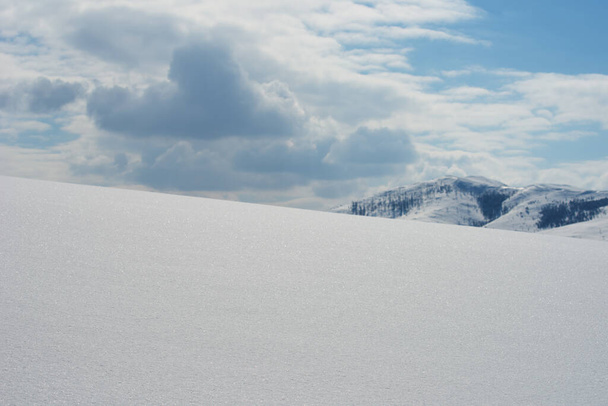 Empty hill under pure white snow in winter as copy space, mountain and clouds in background - Photo, image