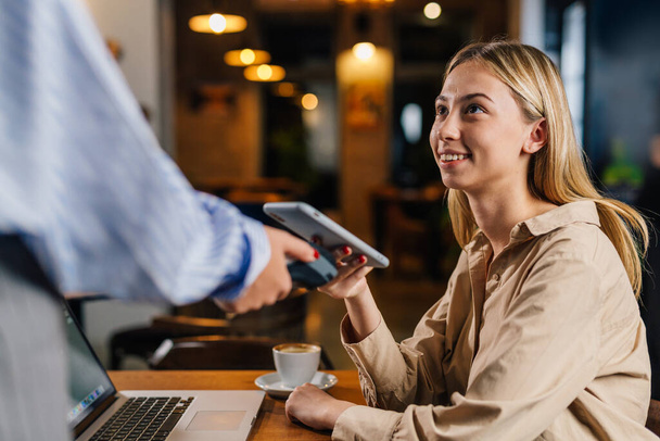 Young woman pays her bill contactless - 写真・画像