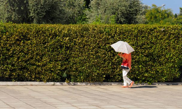Neznámá žena držící slunečník, aby se chránila před sluncem procházejícím se ulicí. Atény Řecko - Fotografie, Obrázek