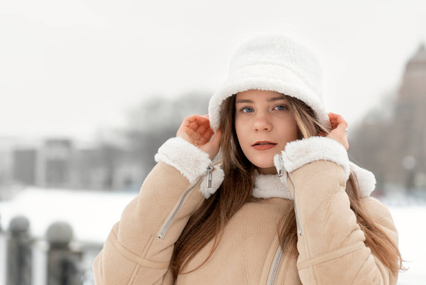 Портрет стильной девушки в модной меховой белой панаме и бежевом овечьем пальто. Молодая женщина в модном зимнем виде - Фото, изображение