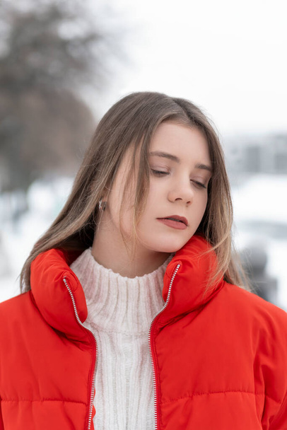 Close-up portrait of cute girl with light makeup in red jacket in winter outside. Warm womens clothing for walking. - Photo, Image