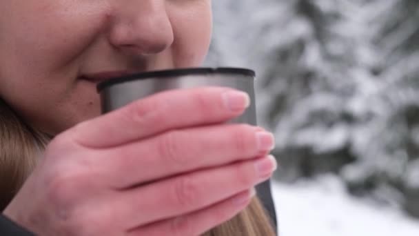Primer plano de la atractiva joven bebiendo café caliente o té del termo en el bosque nevado de invierno. Concepto de vacaciones de invierno. - Metraje, vídeo